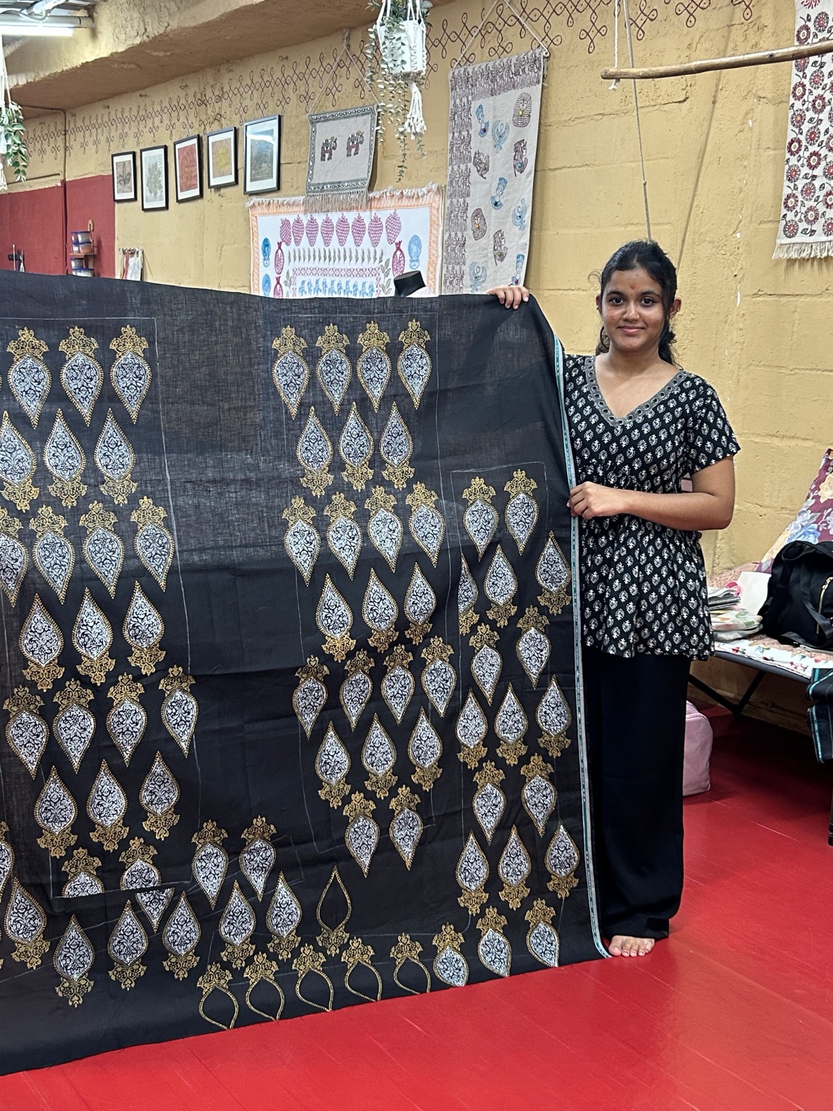 A design student standing beside a long black fabric block printed with white and grey paisley motifs